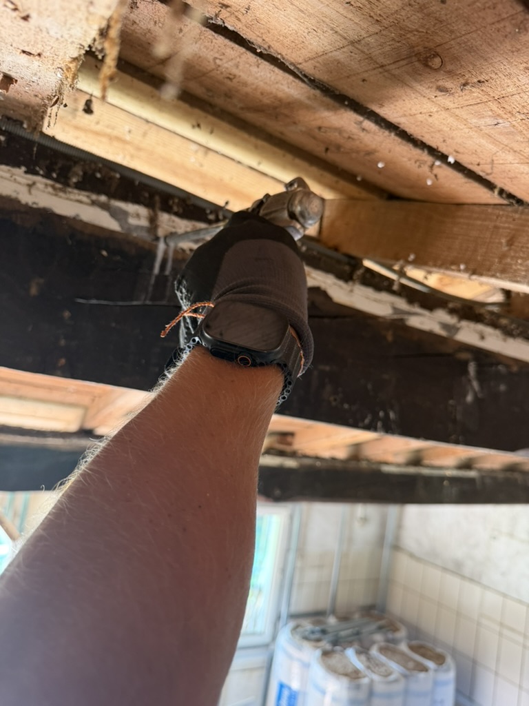 Technicien intervenant avec un outil sur une poutre sous un plancher en bois