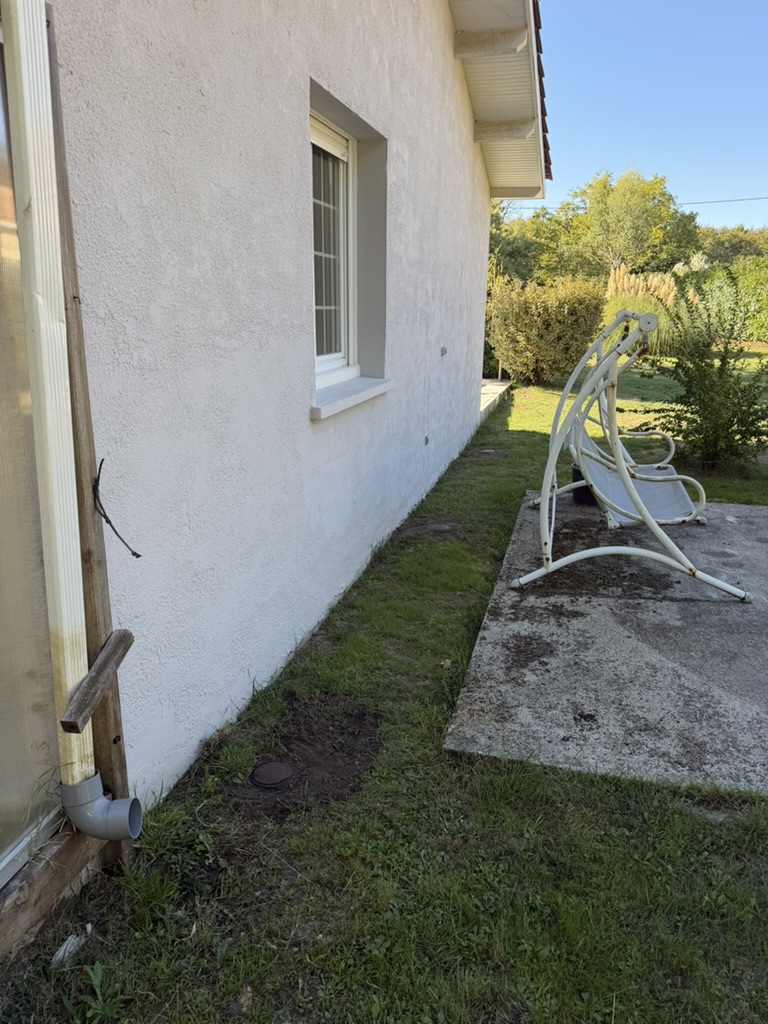 Couvercle d'une station au sol près de la façade et de la descente de gouttière d'une maison