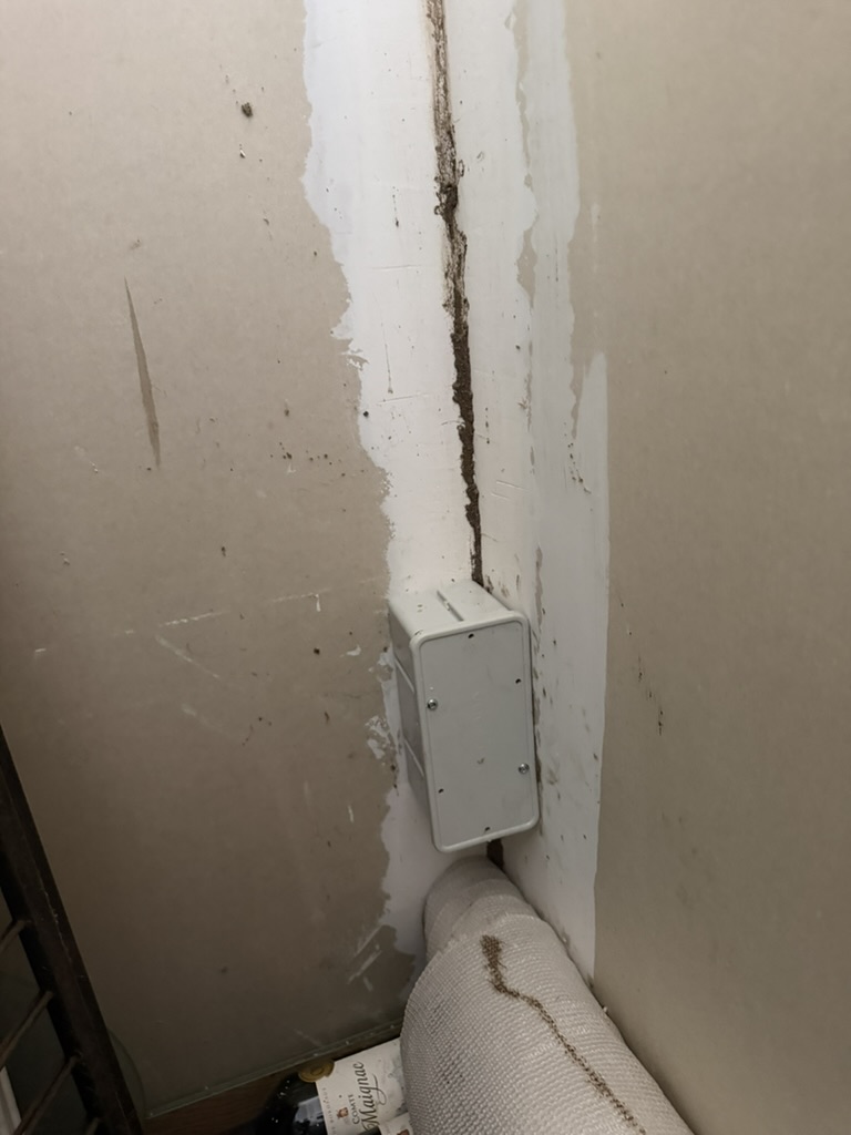Boîtier anti-termites fixé dans un angle de mur le long de cordonnets terreux